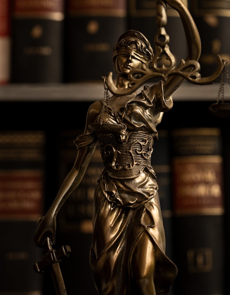 Close-up of a golden Lady Justice statue with scales in a law library setting.